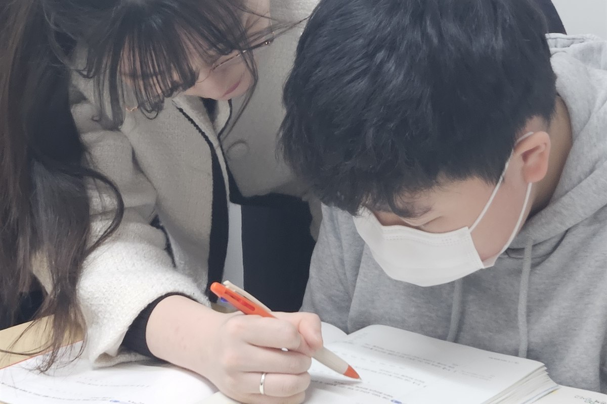 백마 초등수학학원 민주쌤이 초등학생 옆에서 문제를 짚어가며 개인별 맞춤으로 지도하는 모습